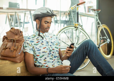 Mann in Fahrradhelm mit Handy im Büro Stockfoto