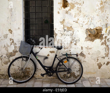 Traditionellen Fahrrad eine rustikale, bröckelnden, weiß getünchten Wand in einer alten spanischen Straße mit Kopfsteinpflaster und einem Fenster gelehnt Stockfoto