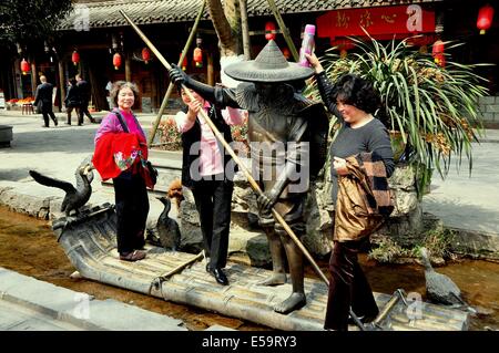 JIE ZI antiken Stadt (SICHUAN), CHINA: Drei Frauen Besucher posieren mit einem Bootsmann auf einem Floß-Skulptur Stockfoto