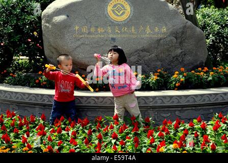 JIE ZI ANCIENT TOWN, CHINA: Zwei kleine Kinder Seifenblasen vor einem Felsblock Stockfoto