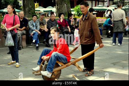 JIE ZI ANCIENT TOWN, CHINA: Junges Mädchen bekommt eine Fahrt in einer einzigartigen chinesischen Stil aus Holz Schubkarre entlang der Straßen der Stadt Stockfoto