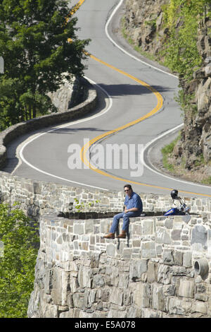 Stadt von Deerpark, New York, USA. 24. Juli 2014. Ein Motorradfahrer sitzt auf einer Felswand und nimmt in der Ansicht auf das Hawk Nest Abschnitt der Route 97 in der Stadt Deerpark, New York. Diese kurvenreiche Abschnitt der Straße, befindet sich Hunderte von Fuß über den Delaware River, wurde häufig in TV-Werbespots und Anzeigen verwendet und ist Bestandteil der oberen Delaware Scenic Byway. Bildnachweis: Tom Bushey/ZUMA Draht/Alamy Live-Nachrichten Stockfoto