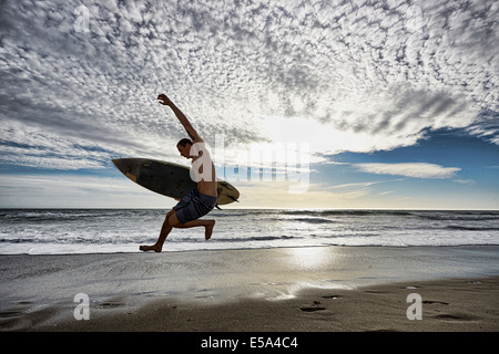 Kaukasischen Mann springt mit Surfbrett am Strand Stockfoto