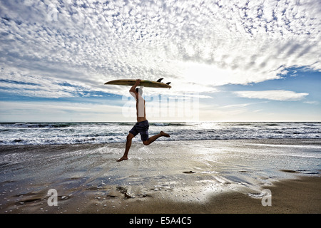 Kaukasischen Mann springt mit Surfbrett am Strand Stockfoto