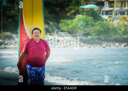 Älteren Hispanic Mann mit Surfbrett am Strand Stockfoto