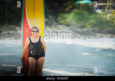 Ältere Hispanic Frau mit Surfbrett am Strand Stockfoto