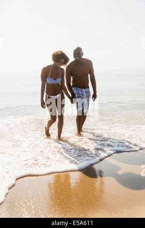 Paar halten Hände in Wellen am Strand Stockfoto