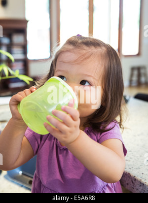 Gemischte Rassen Mädchen trinken aus sippy Tasse in Küche Stockfoto