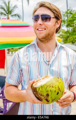 Kaukasischen Mann aus Kokosnuss am Strand trinken Stockfoto