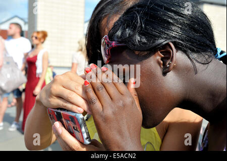 Zwei junge Frau Bildschirm betrachten, auf Smartphone, Abschirmung Bildschirm von Sonne mit Händen, UK Stockfoto