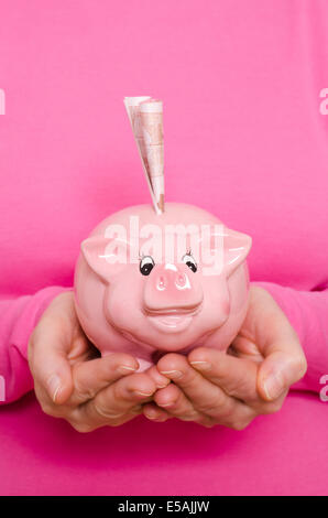 Weibliche Hände halten ein rosa Sparschwein mit 50 Euro-Schein Stockfoto