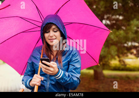 Junge Frau SMS auf Handy im Regen, Debica, Polen Stockfoto