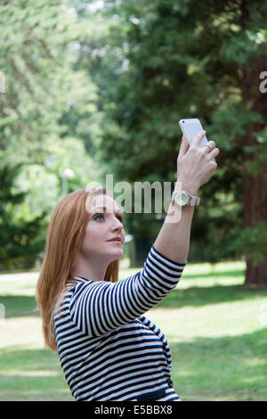 Ein schöne rote kurzhaarige Mädchen nimmt eine "Selfie" mit ihrem Handy und Posen mit einem Lächeln Stockfoto