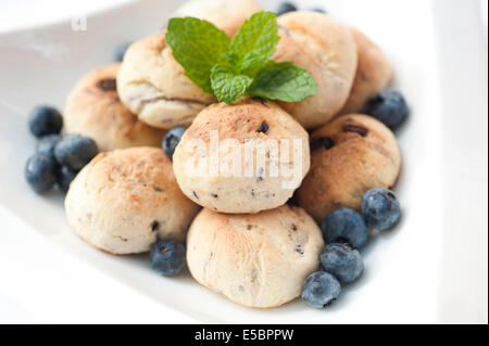 Handgemachte Heidelbeere Cookies mit frischen Heidelbeeren um gelegt und Minzblatt platziert an der Spitze in einer weißen Schüssel auf einem weißen Zeitmessung Stockfoto