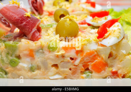 Nahaufnahme einer Platte mit spanischer Ensaladilla Rusa, russischer Salat, garniert mit Serrano-Schinken, Oliven, gekochtes Ei und Paprika Stockfoto