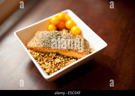 Eine Alaska-Wildlachs gegrillt und gewürzt auf einem Zeder-Brett auf Couscous mit Tomaten auf einem Holztisch platziert. Stockfoto