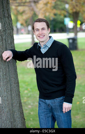 Eine attraktive junge männliche Model posiert durch einen Baum, einen Pullover und eine Schaltfläche zermürben. Stockfoto