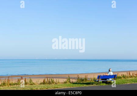 Mann sitzt auf einer Bank am Strand von Thornton Cleveleys in den frühen Morgenstunden, North Blackpool, Lancashire, UK Stockfoto