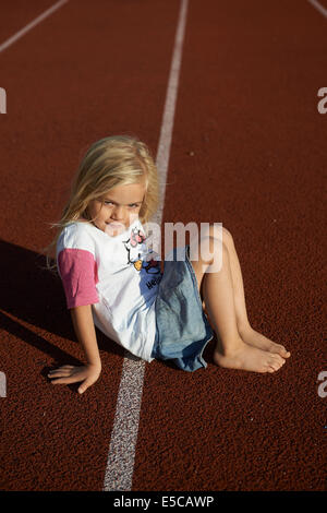 Kind etwas blondes Mädchen sitzen auf Tartan Laufstrecke im Stadion Stockfoto