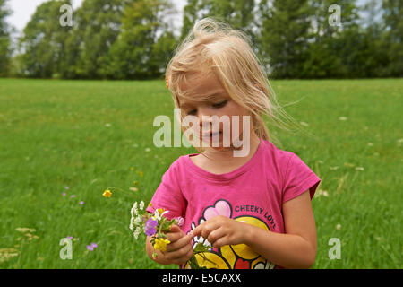 Kleines Kind blonde Mädchen auf der Wiese mit Blumen Stockfoto