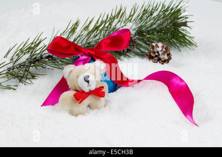 Closeup Vorderansicht des kleinen Pelz Bär mit Schnee bedeckt, Tanne Zweig, rote Schleife und Tannenzapfen im Hintergrund Stockfoto