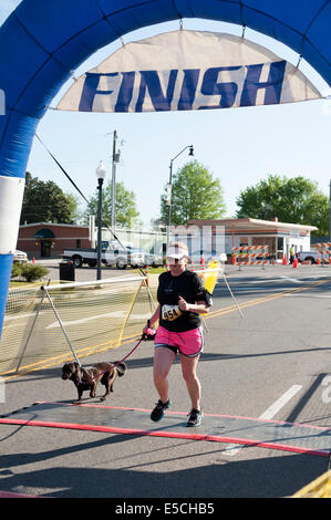 Frau in 5K oder 10K Marathon Rennen Kreuzung Ziellinie mit einem Hund an der Leine Stockfoto