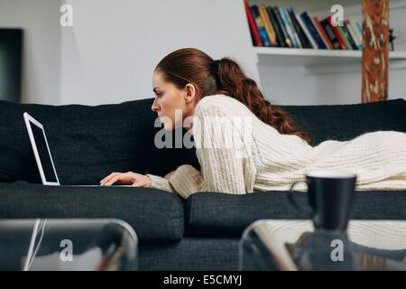 Seitenansicht der jungen Dame auf Sofa mit einem Laptop-Computer zu Hause. Schöne junge Dame am Laptop arbeiten. Stockfoto