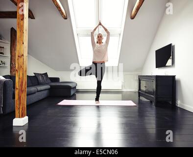 Voller Länge Bild Fit jungen Frau stehen auf einem Bein und meditieren in ihrem Wohnzimmer. Kaukasischen Frauen Yoga zu Hause zu tun. Stockfoto