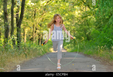 kleines Mädchen springt über Seil im Wald Stockfoto