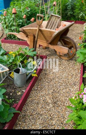 Blick auf kleine Hochbeet Pflanzen mit Sommerkulturen und traditionellen hölzernen Schubkarre, England Juli. Stockfoto