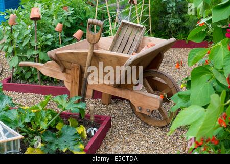 Blick auf kleine Hochbeet Pflanzen mit Sommerkulturen und traditionellen hölzernen Schubkarre, England Juli. Stockfoto