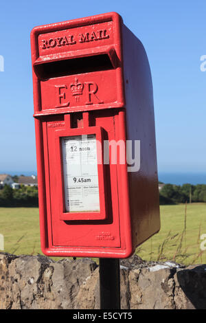 Neu lackiert, wonky rot Royal Mail Briefkasten gelehnt seitlich blauen Himmel. Benllech, Isle of Anglesey, North Wales, UK, Brit Stockfoto