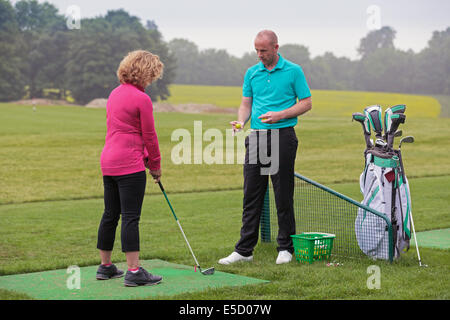 Eine Dame Golfer gelehrt von einem Profi auf eine Praxis, die driving-Range, Golf zu spielen. Stockfoto