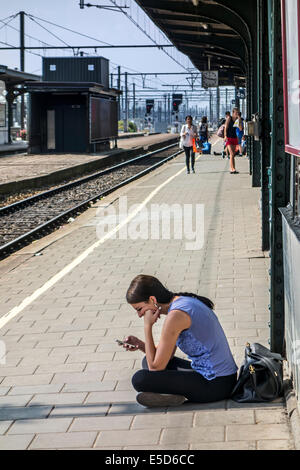 Gelangweilt Mädchen mit Smartphone warten auf verspätete Zug am Bahnsteig im Bahnhof Stockfoto