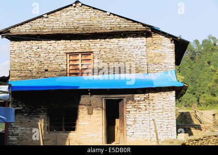 Ummauerten traditionellen nepalesischen Bauernhaus aus Stein mit blauen Kunststoff Fringe und Holzfenster und Tür in Dhampus Dorf auf der Anna Stockfoto