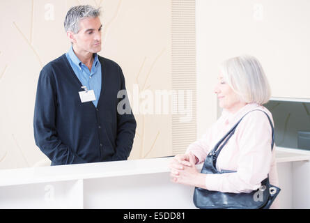 Männliche Angestellte an der Rezeption empfangen senior Frau an der Rezeption im Krankenhaus Wartezimmer. Stockfoto