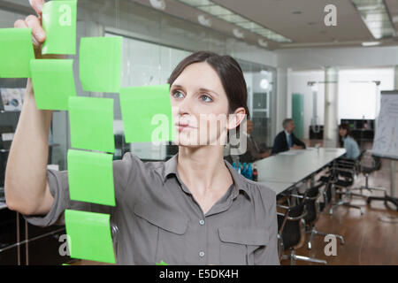 Deutschland, München, Geschäftsfrau im Büro, indem Haftnotizen auf Glasscheibe Stockfoto