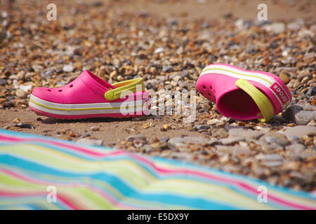 Rosa Crocs verworfen am Strand neben dem stripey Strandtuch Stockfoto