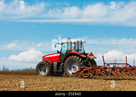 Der Bauer das Feld pflügen. Traktor im Bereich Pflege. Roter Traktor mit einem Pflug in einem Bauernhof-Feld. Traktor und Pflug Stockfoto