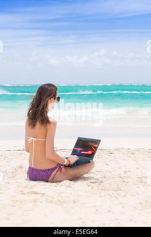 Eine junge Frau mit einem Laptop am Strand in der Karibik Stockfoto
