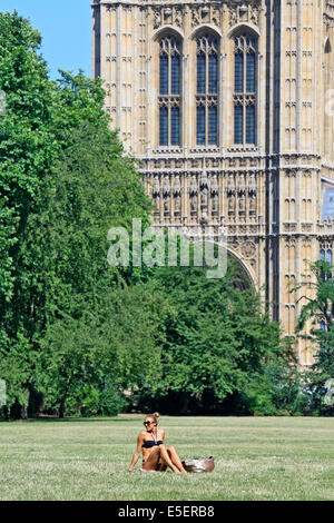 Eine schöne junge Frau Sonnenbaden neben den Houses of Parliament, in Victoria Tower Gardens, Westminster, London, Großbritannien Stockfoto