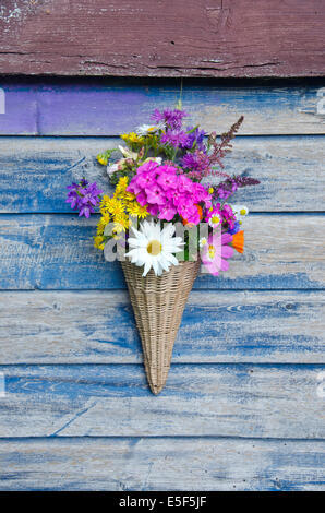 schöne Blumen in Weidenkorb auf alte Holzwand Stockfoto