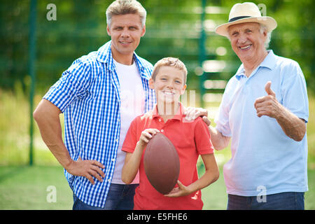 Süsser Boy mit Rugby-Ball und seinem Großvater und Vater Blick auf Kamera im freien Stockfoto