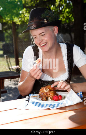 Blonde Mädchen isst halbe Hähnchen in einem traditionellen bayerischen Biergarten Stockfoto