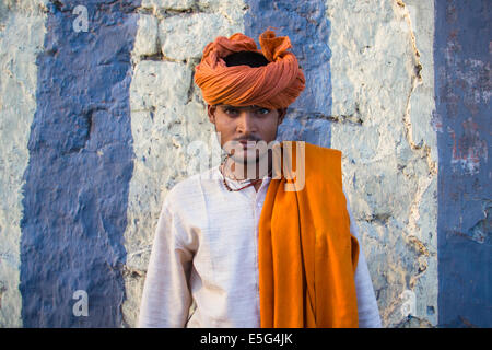 Bunte hindu Jüngling, mit einem orangefarbenen Turban posiert vor einer gestreiften Wand im alten Teil von New Delhi, der Hauptstadt von Indien.