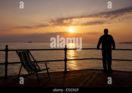 Hampton in der Nähe von Herne Bay, Kent, UK 31. Juli 2014. Eine trübe Sonnenaufgang in Hampton in Kent. Ein Mann schaut die Ansicht mit den Ruinen von Herne Bay Pier sichtbar, die von Stürmen in den 1970er Jahren zerstört worden war. Das sonnige Wetter wird voraussichtlich bis Samstag bleiben beim Duschen für den Südosten prognostiziert werden. Stockfoto