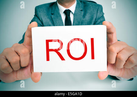 Geschäftsmann, sitzen in einem Schreibtisch zeigt ein Schild mit dem Text ROI, ROI, Akronym für Zinssatz oder Return on Investment, Stockfoto