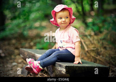 Kleine Mädchen sitzen auf der Bank im Wald Stockfoto