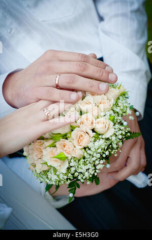 Braut und Bräutigam die Hände mit Trauringe auf Bouquet. Schwerpunkt liegt auf der Seite des Bräutigams Stockfoto