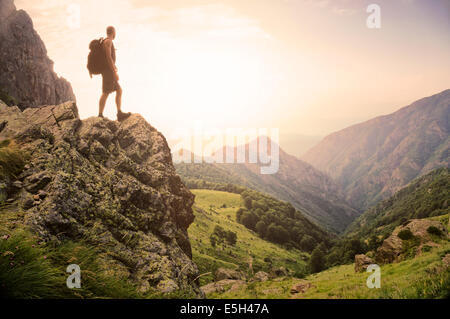 Gesunde junge Mann steht auf einem Felsen hoch in den Bergen, genießen Sie die natürliche Schönheit im Morgenlicht. Stockfoto
